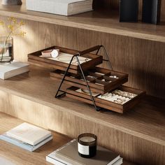 a wooden shelf with two trays and books on top of it next to a vase