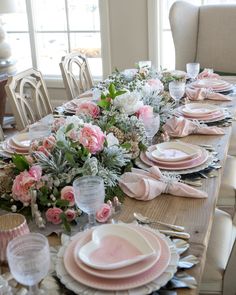 the table is set with pink and white plates, silverware, and floral centerpieces