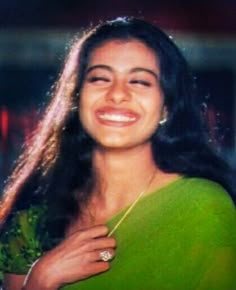 a woman in a green sari smiling at the camera with long hair on her head