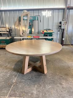 a round wooden table sitting inside of a garage next to machines and tools on the floor