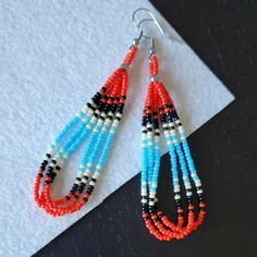 These teardrop beaded earrings are made with stainless steel findings, and three hanging loop strands of Japanese Miyuki and/or Czech beads. Most earrings I make in this style have a pattern in groups of fours or sevens. Four being for the four directions, and seven being for the seven clans of my tribe.  Colors used in this design are red, baby blue, black, and bone white. From top of hook to bottom bead is approximately 3.5" long.  Hooks are stainless steel and come with clear backings.  Nicke Teardrop Polished Bead Earrings For Gifts, Teardrop Polished Beads Earrings For Gift, Teardrop Earrings With Polished Beads For Gift, Dangle Teardrop Earrings With Tiny Beads, Dangle Teardrop Earrings With Tiny Beads As Gift, Gift Teardrop Dangle Earrings With Tiny Beads, Beaded Ladder Stitch Hoop Earrings Native American, Cab Earrings Native American, Southwestern Style Blue Beaded Earrings