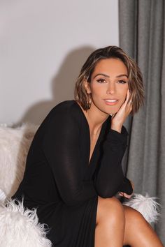 a woman sitting on top of a white couch wearing a black dress and holding her hand to her face