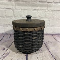 a black basket with lid sitting on top of a wooden table next to a white brick wall