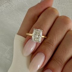 a woman's hand holding a ring with a square diamond in the middle and a white background