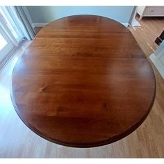 a round wooden table in the middle of a room with hard wood floors and white walls