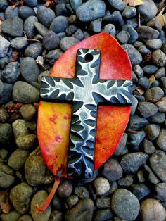 a metal cross sitting on top of a pile of rocks next to leaves and stones