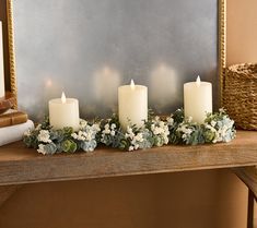 candles are lit on a mantle with flowers and greenery