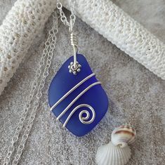 a blue sea glass pendant sitting on top of a white piece of cloth next to a seashell