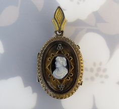 "A carved hardstone cameo is centered on this antique ca. 1880s gold filled locket pendant. The cameo was carved from one black and white stone. The woman is facing left with tiny features, ornate curls and draped clothing. Raised geometric elements with textured detailing frame the cameo. A decorative trim flows around the oval face. The top is fitted with a fancy bail. The locket opens with two pull tabs on the side. Inside are two tin types of a man and woman (who could resemble the cameo). T Antique Cameo Medallion Jewelry, Victorian Cameo Locket Necklace As A Gift, Victorian Cameo Jewelry, Cameo Medallion Locket Necklace, Victorian Cameo Oval Locket Necklace, Victorian Cameo Pendant Jewelry, Victorian Oval Cameo Locket Necklace, Victorian Cameo Locket Necklace For Formal Occasions, Antique Brass Cameo Locket Necklace