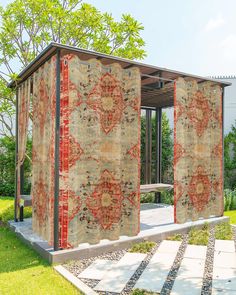 an outdoor area with a covered bench and rugs on the walls, in front of trees