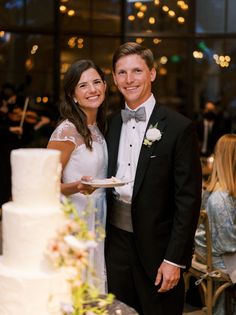 a man and woman standing next to each other in front of a white wedding cake