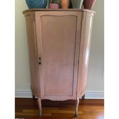 an old pink cabinet with vases on top