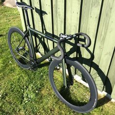 a bicycle parked next to a green fence in the grass near a wooden fence with black spokes