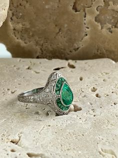 Item Details Model Number: SDL2000BWY Metal: Platinum 850 Weight: 5.2 grams Length: 17 mm (face of ring) Style: Art Deco Ring Size: 7 (contact us for sizing options) Main Stone Details Main Stone: Emerald Carat Weight: 1.2 CT, 0.45 CT Shape: Pear, French Cut Color/Clarity: Green/ Certificate: GGA All of our diamonds and gemstones are 100% natural! Other Diamond Details Carat Weight: 0.18 CT Shape: Round Color/Clarity: F/SI1 Cut: Excellent Green Certificate, Platinum Diamond Ring, Style Art Deco, Platinum Diamond Rings, Emerald Diamond Ring, French Cut, Studded Necklace, Eternity Band Ring, Deco Ring