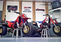 two red and blue dirt bikes sitting on top of metal stands in front of a tv