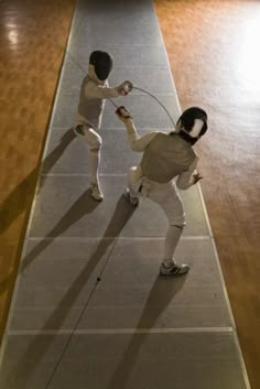 two people in fencing gear standing on a wooden floor with one holding the other's hand