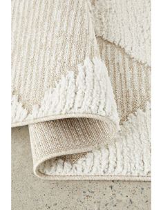 a white rug on the floor next to a beige and white rug with fringes