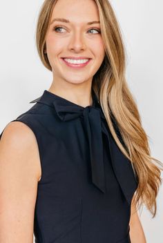 a woman with long hair wearing a black dress and smiling at the camera while standing in front of a white background