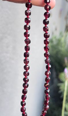 a hand holding a strand of red glass beads