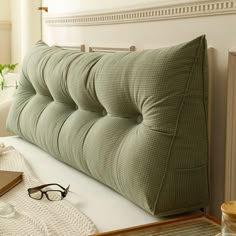 a green pillow sitting on top of a bed next to a pair of eyeglasses