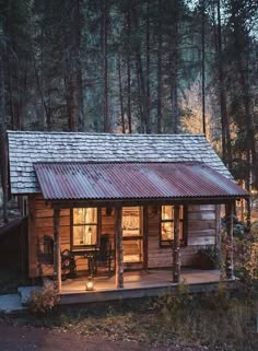 a small cabin in the woods with a porch and covered veranda area at night