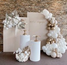 a table topped with white and gold balloons next to a greeting card, vases and candle holder