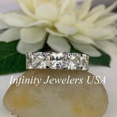 three stone ring sitting on top of a rock next to a white flower with the words infinity jewelers usa