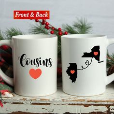 two white coffee mugs with the words sisters and heart on them sitting next to evergreen branches