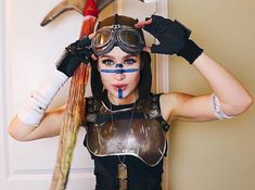 a woman with painted face and goggles is holding her hair in the air while standing next to two birds