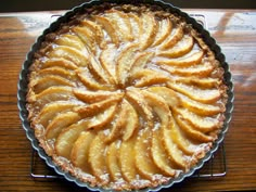 a pie sitting on top of a wooden table next to a pan filled with apples