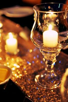 candles are lit in a glass vase on a table