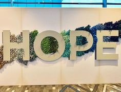 a sign that says hope in front of a wall with trees and bushes on it