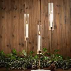 three candles are lit on a table with greenery