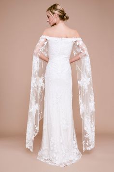 a woman in a white wedding dress with an off the shoulder cape