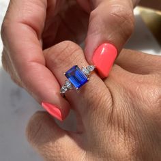 a woman's hand with pink and blue nail polish holding an engagement ring in her left hand