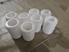 several white vases sitting on top of a brown cloth covered tablecloth, all lined up in the same row