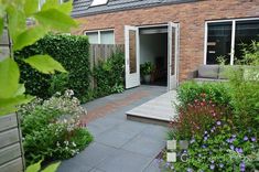 a brick house with an open door and garden area in the foreground, surrounded by greenery