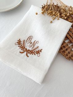 a white table cloth with a monogrammed initial on it next to a wicker basket