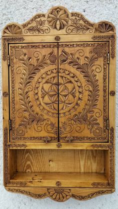 an old wooden cabinet with carvings on the front and side panels, hanging on a wall