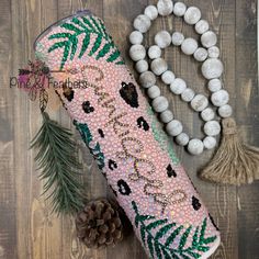 the beaded case is next to pine cones and beads on a wooden surface with a pine cone