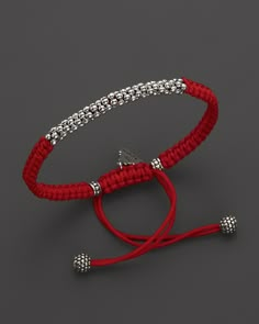 a red rope bracelet with silver beads and two balls on it's end, against a gray background