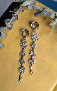 two pairs of silver earrings sitting on top of a yellow table next to green leaves