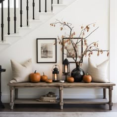 a wooden table topped with two vases filled with orange pumpkins next to a stair case