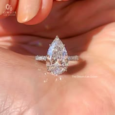 a woman's hand holding an engagement ring with a pear shaped diamond