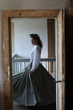 a woman in a white shirt and green skirt is standing on a porch with an open door