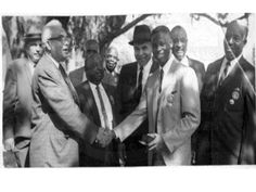 a group of men standing next to each other in front of a tree wearing suits and ties