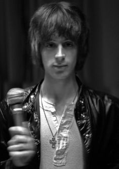 a young man holding a microphone in his right hand and wearing a leather jacket on