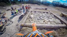 a group of people standing around a dirt bike track with rocks and logs on the ground