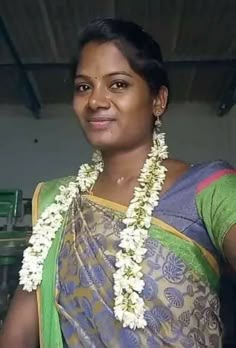 a woman wearing a green and blue sari with white flowers on her neck is smiling at the camera