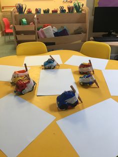 children's toy cars are sitting on top of construction paper at a table in a classroom